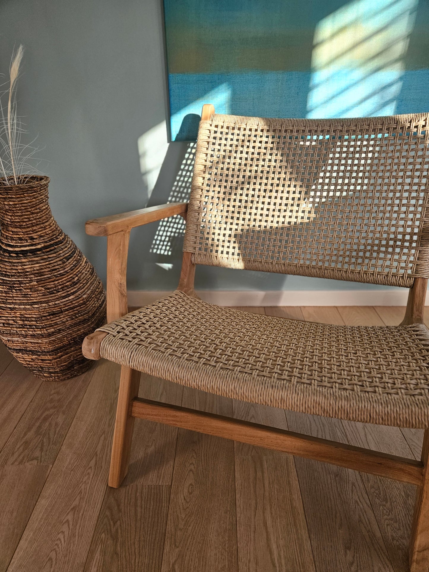 Sillón lounge Tropézienne que muestra su estructura de teca y asiento de ratán tejido en un espacio luminoso de sala de estar