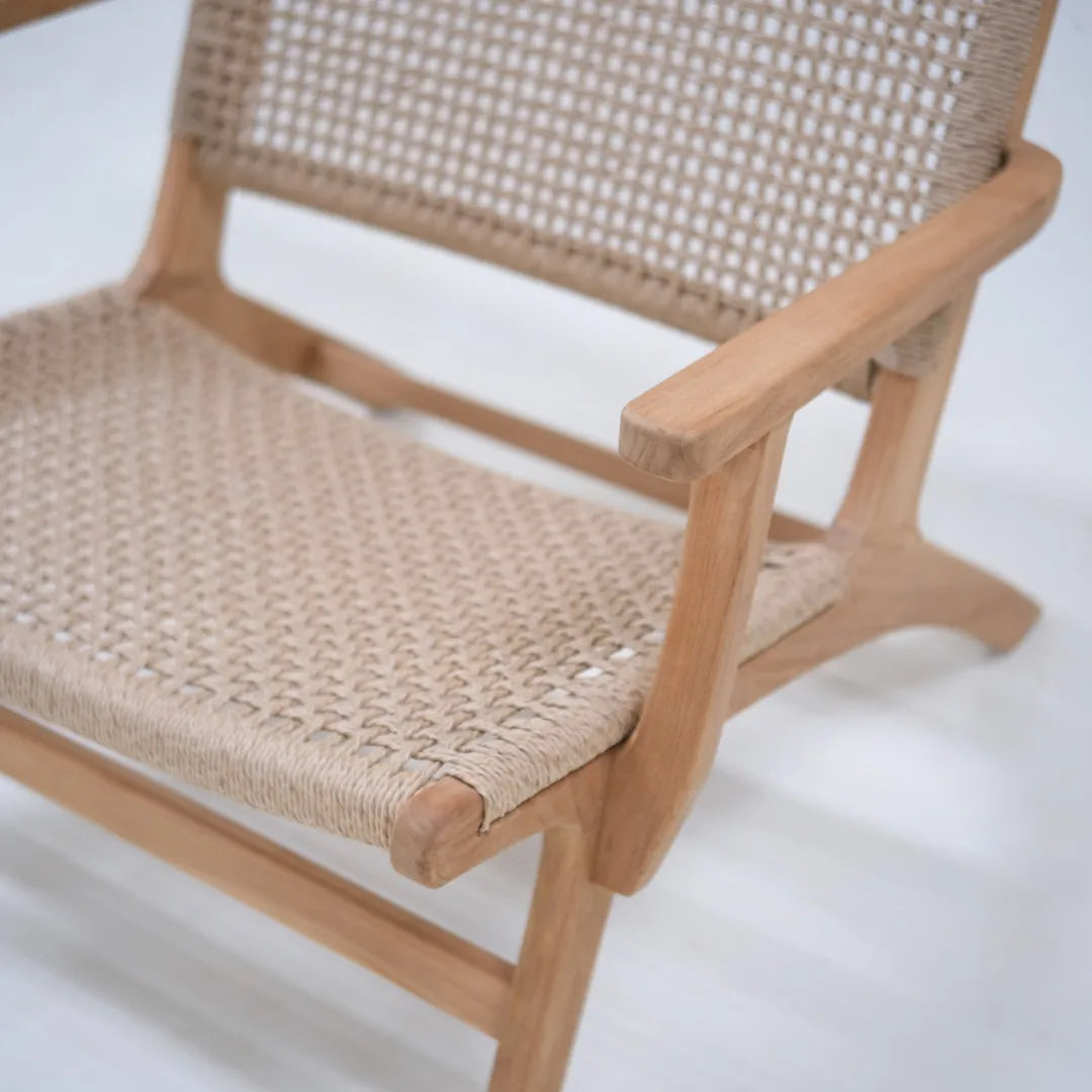 Primer plano del reposabrazos de teca del sillón lounge Tropézienne y del asiento de ratán tejido a mano.