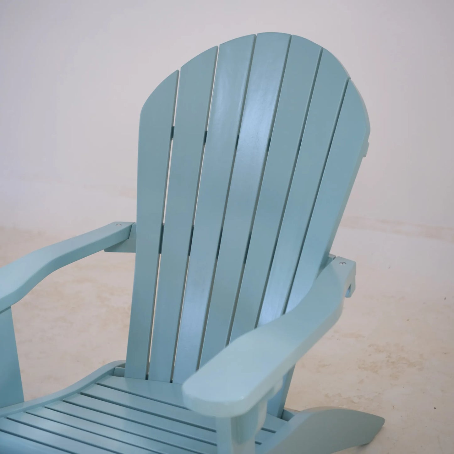Close-up of the pastel blue Adirondack chair showing the curved slatted backrest and wide armrests in smooth painted teak.
