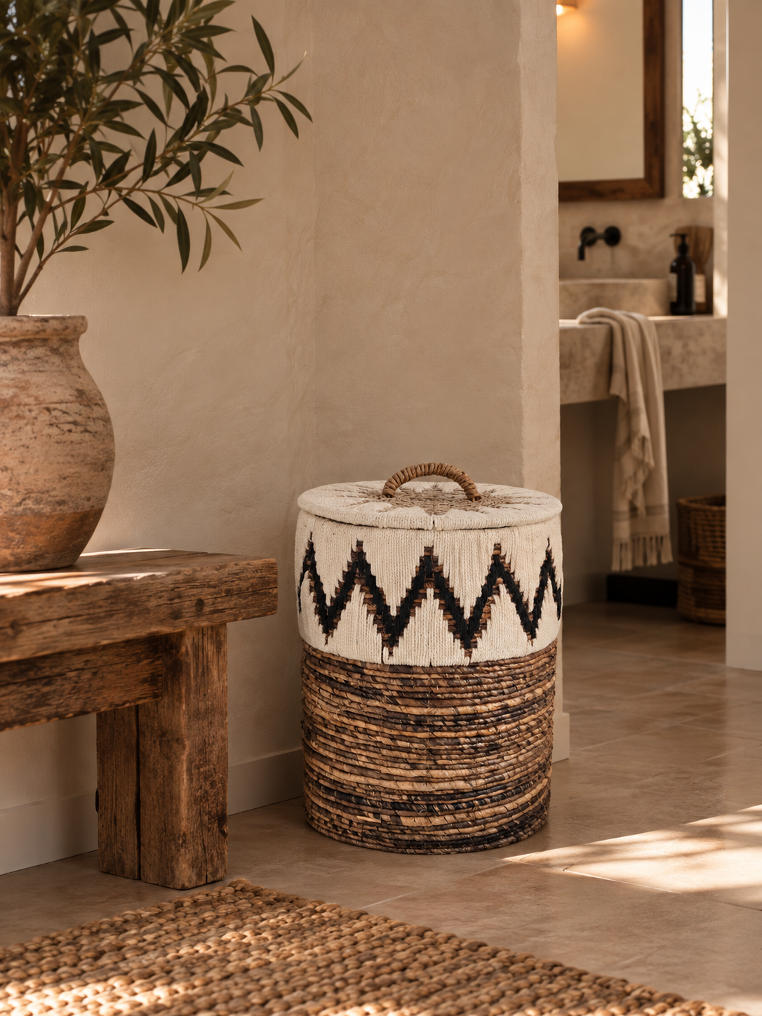 Off-white woven storage basket with a black and natural pattern, braided handle and natural banana-fiber base in a warm Mediterranean interior.