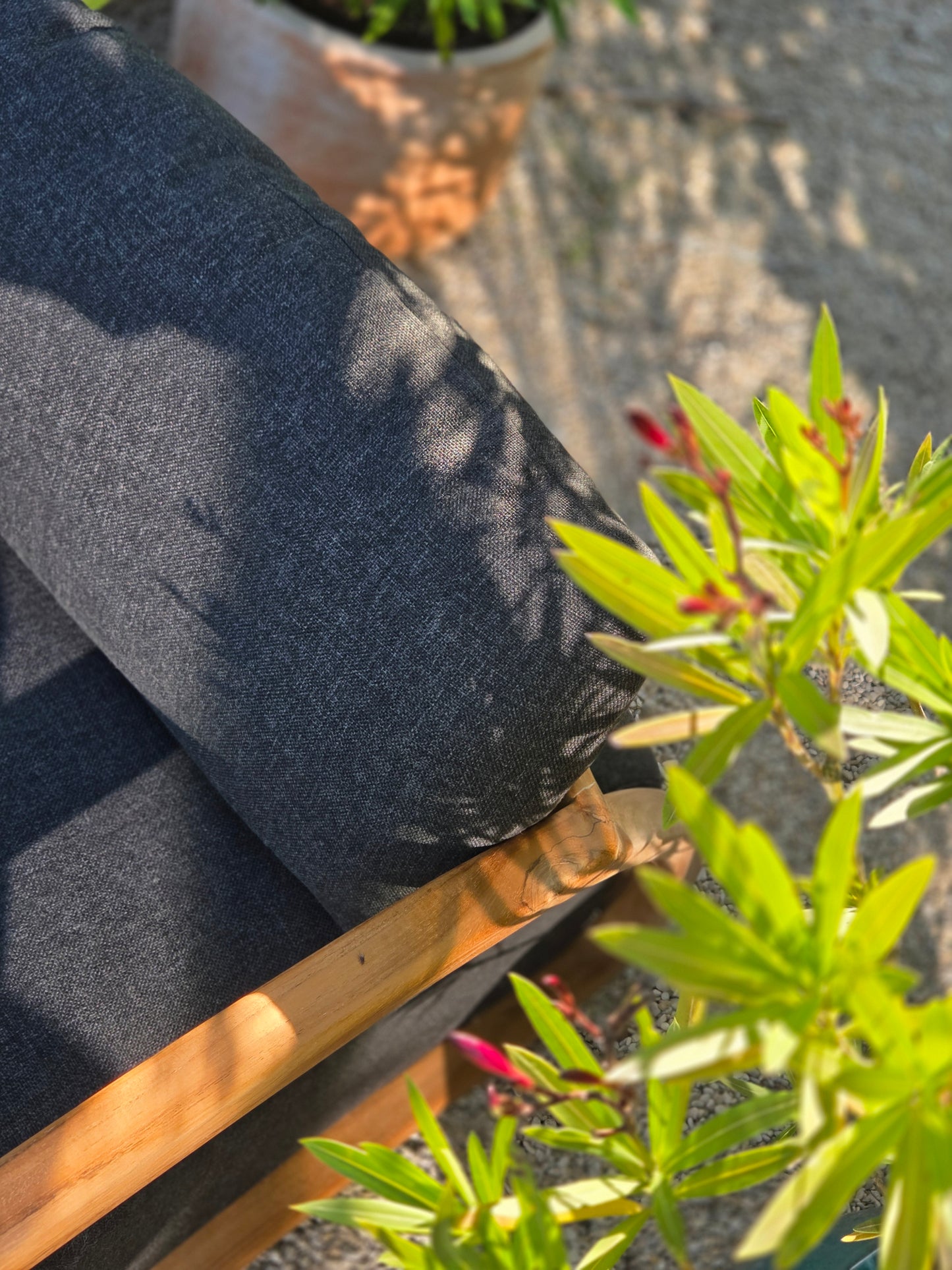 Luxury outdoor lounge chair detail showcasing rich charcoal fabrics, weather-resistant outdoor cushions, natural Grade A teak and warm Mediterranean garden light