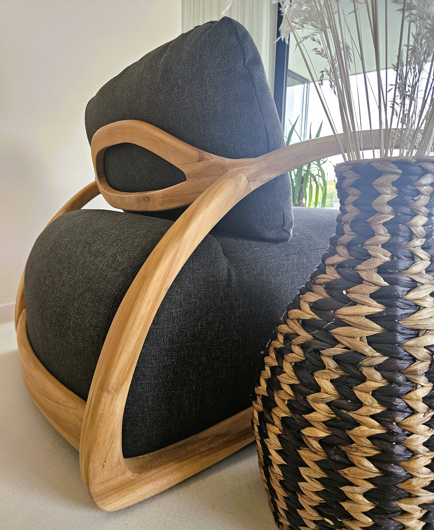 Close-up of a handcrafted wooden lounge chair with dark upholstery, styled beside a woven natural fiber vase in a warm contemporary interior.
