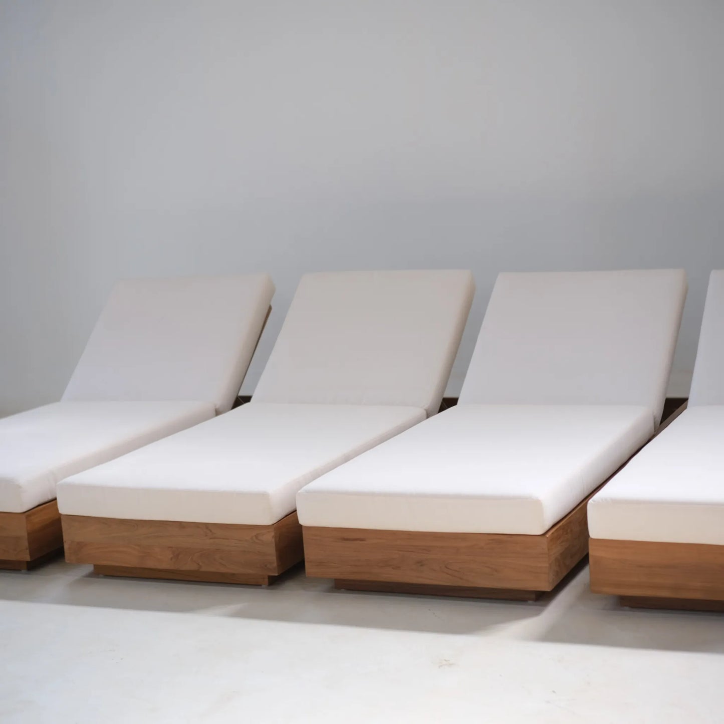 A row of teak Laguna Sun Beds with white cushions arranged in a studio environment.