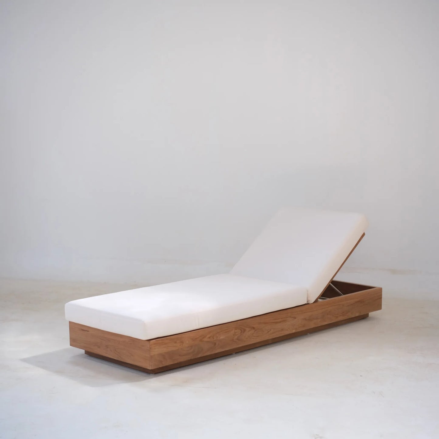 Single Laguna Sun Bed in teak with raised backrest and white cushion, photographed in a minimalist studio.