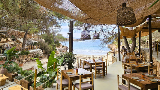 Ibiza beach restaurant with wooden furniture and woven pendant lamps, relaxed boho outdoor dining by the Mediterranean