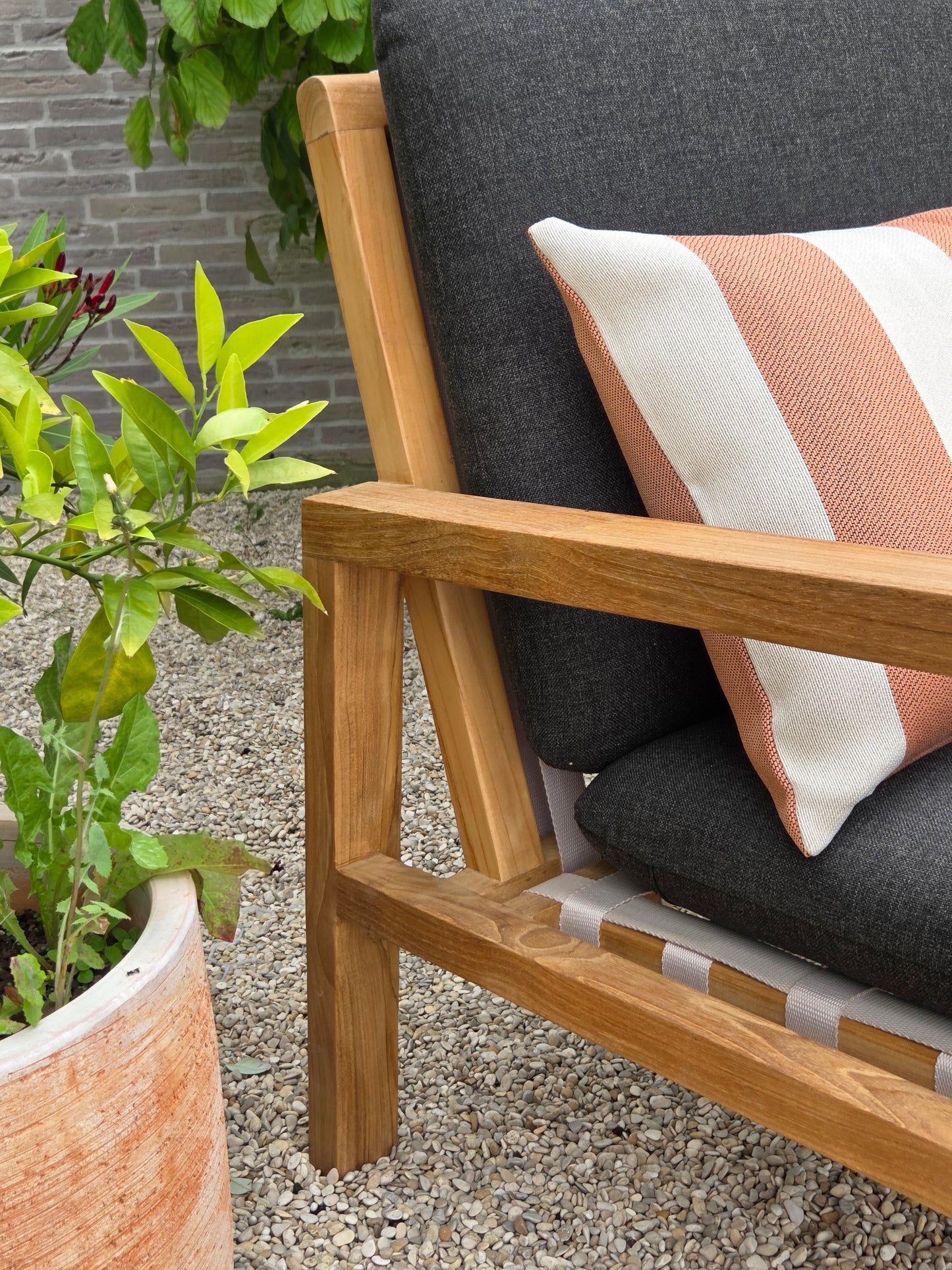 Detailed view of a teak garden lounge chair with weather-resistant charcoal cushions, wooden armrest and woven support straps