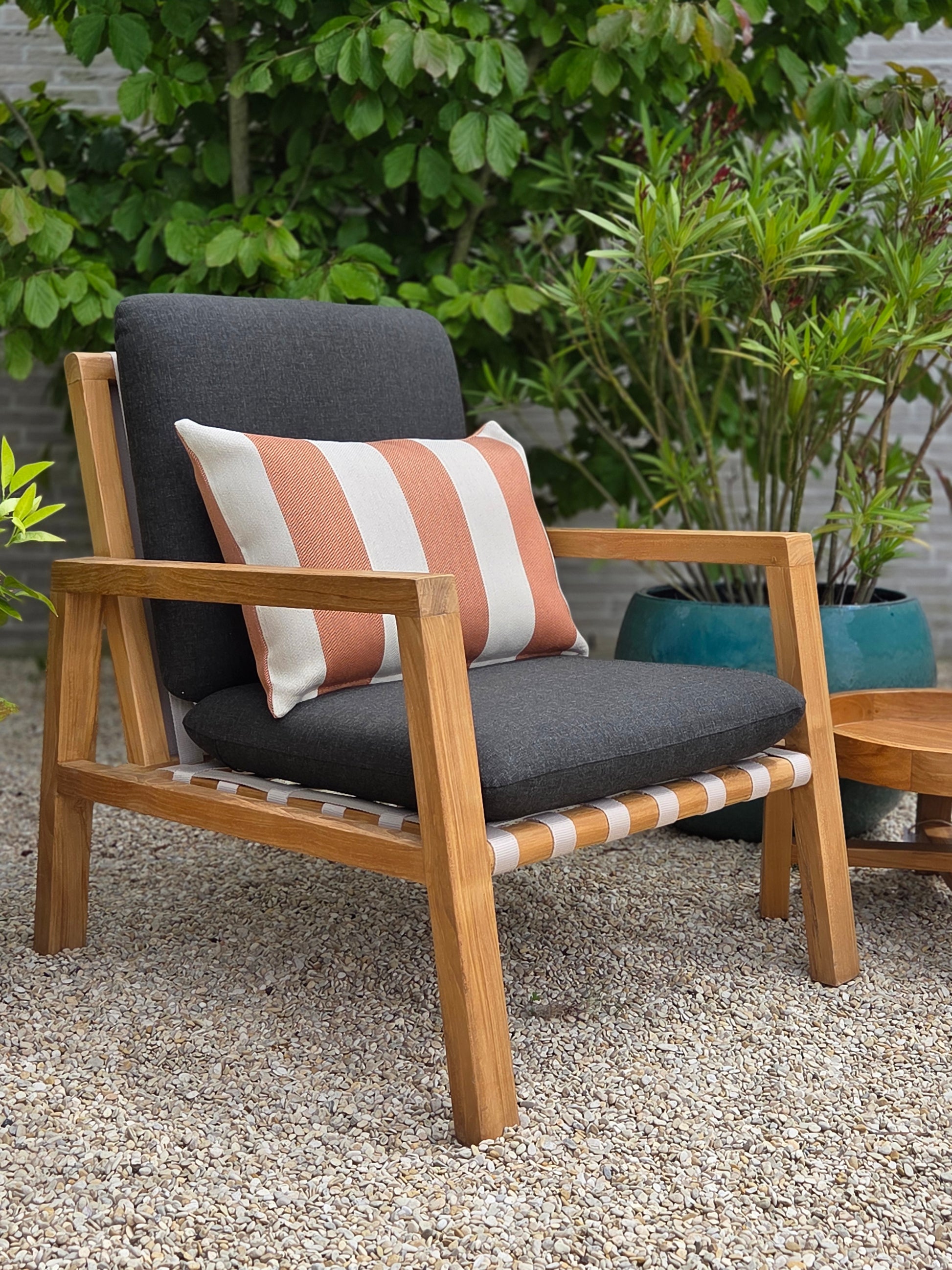 Luxury teak lounge chair with black cushions and striped pillow in a Mediterranean-inspired outdoor garden