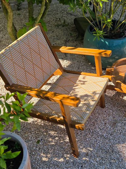 Teak lounge chair with woven rope seat and backrest in a contemporary outdoor garden setting with natural gravel and plants