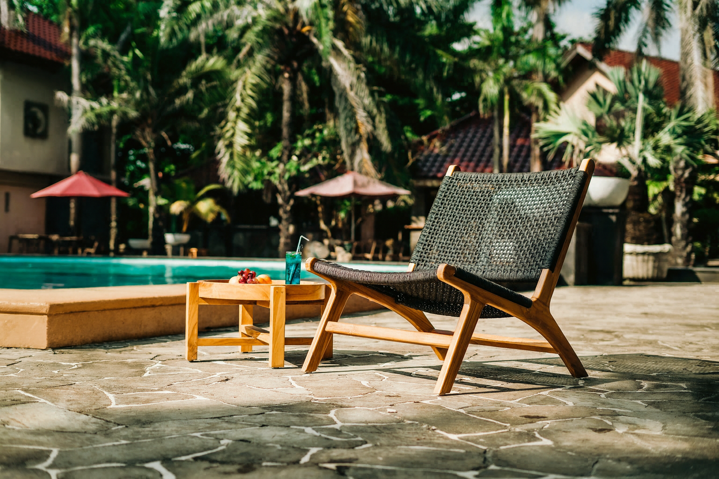 Siga-Siga outdoor lounge chair with a handcrafted teak frame and black synthetic rattan weave, paired with a Formosa teak side table beside a tropical swimming pool.