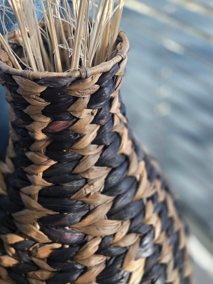 Close-up of the narrow neck and braided rim of a black and natural woven vase, highlighting the contrasting fibres and intricate geometric weave.