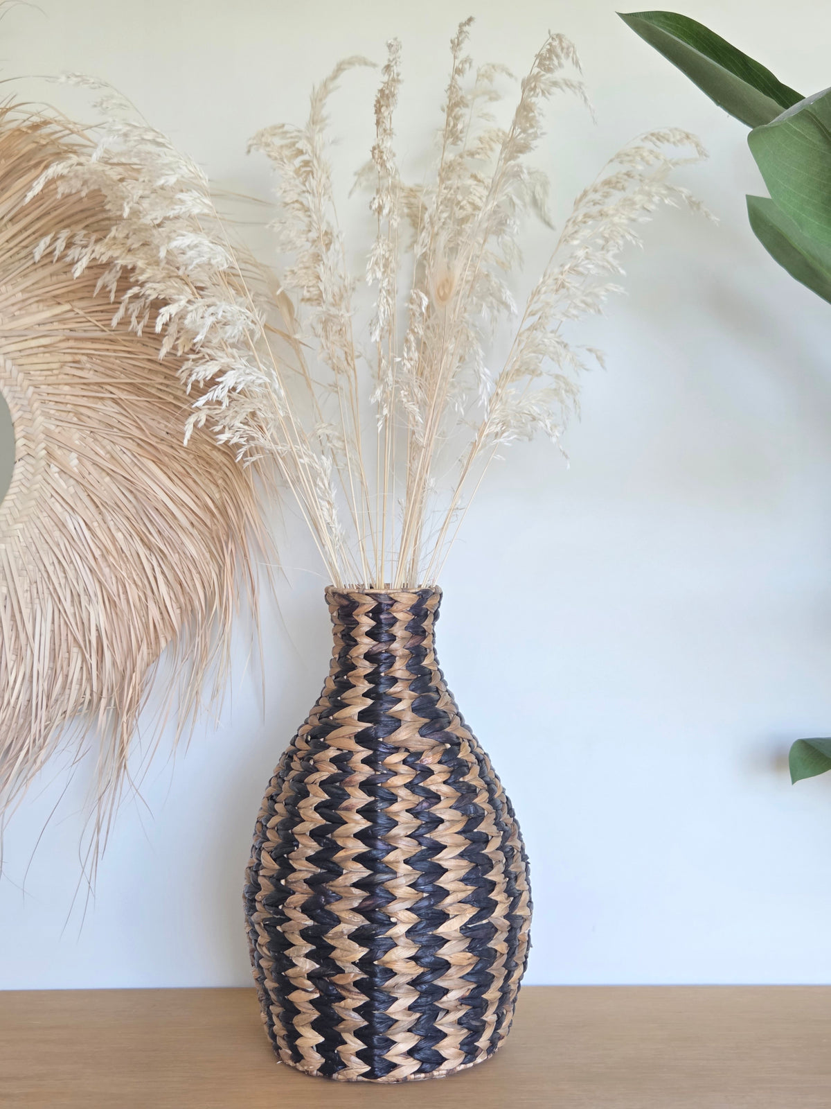 Zahara decorative woven vase with a black and natural zigzag pattern, filled with delicate dried grasses and displayed on a wooden surface in a bright bohemian interior