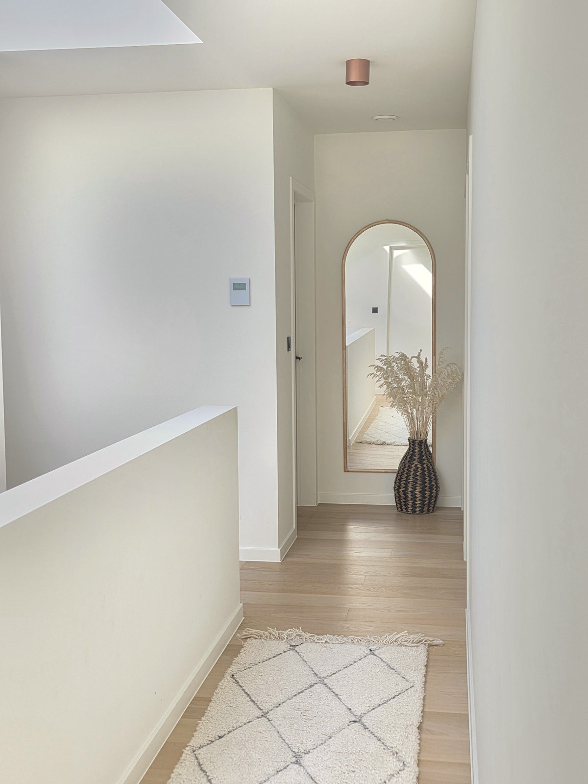 Zahara black and natural woven floor vase with dried grasses, adding bohemian character to a minimalist hallway with light wood flooring and a cream geometric rug