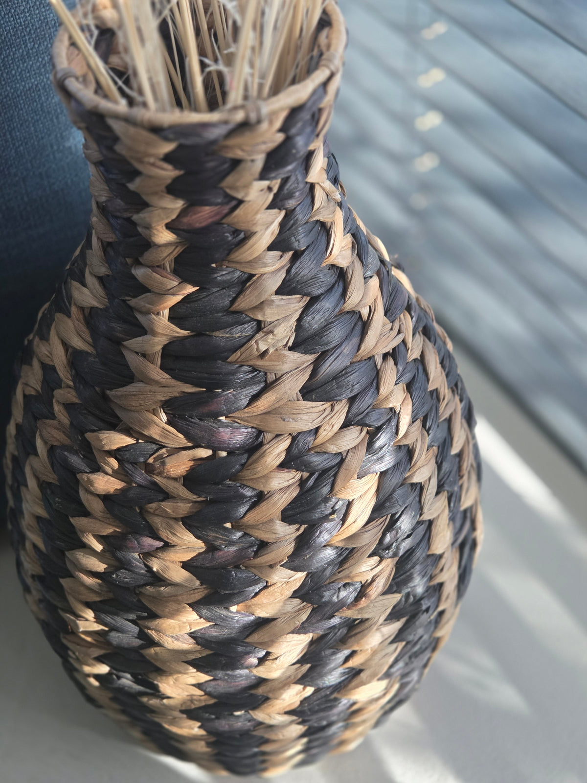 Detailed view of a decorative woven vase featuring a bold black and natural zigzag pattern, a rounded body and a narrow neck with textured braided fibres.