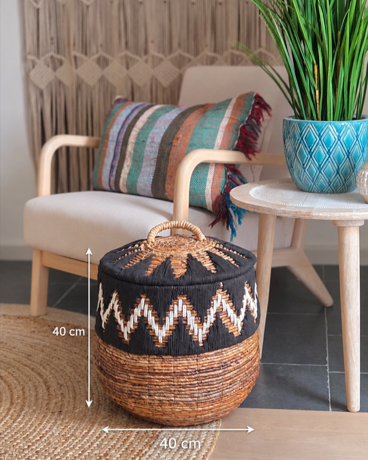 Close-up of a round woven storage basket with lid, featuring a black and white geometric pattern, natural woven base and decorative handle.