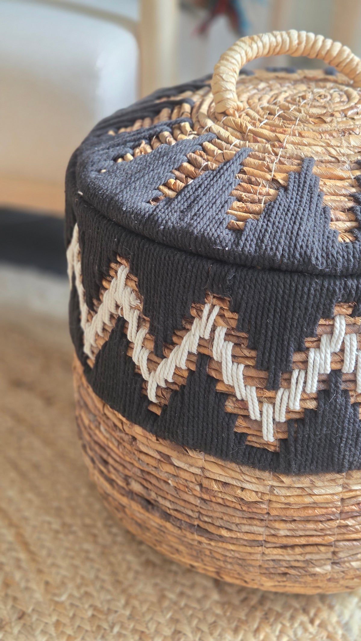 Detailed view of a handcrafted storage basket highlighting the textured black and white geometric weaving, natural fibres and woven lid with handle.