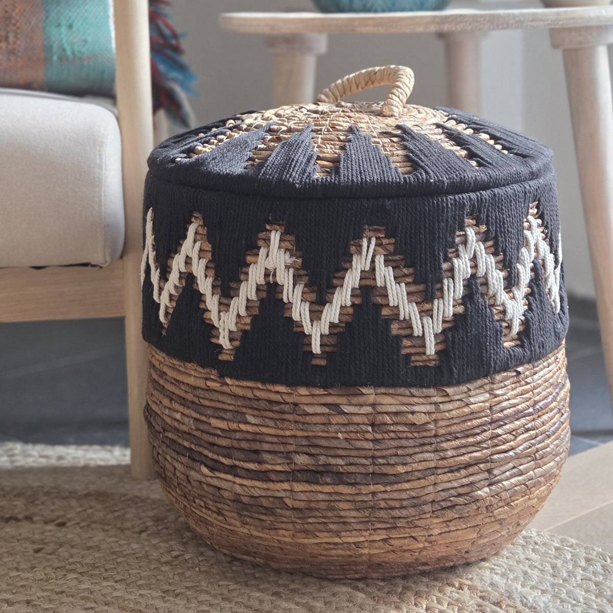 Close-up of a round woven storage basket with lid, featuring a black and white geometric pattern, natural woven base and decorative handle.