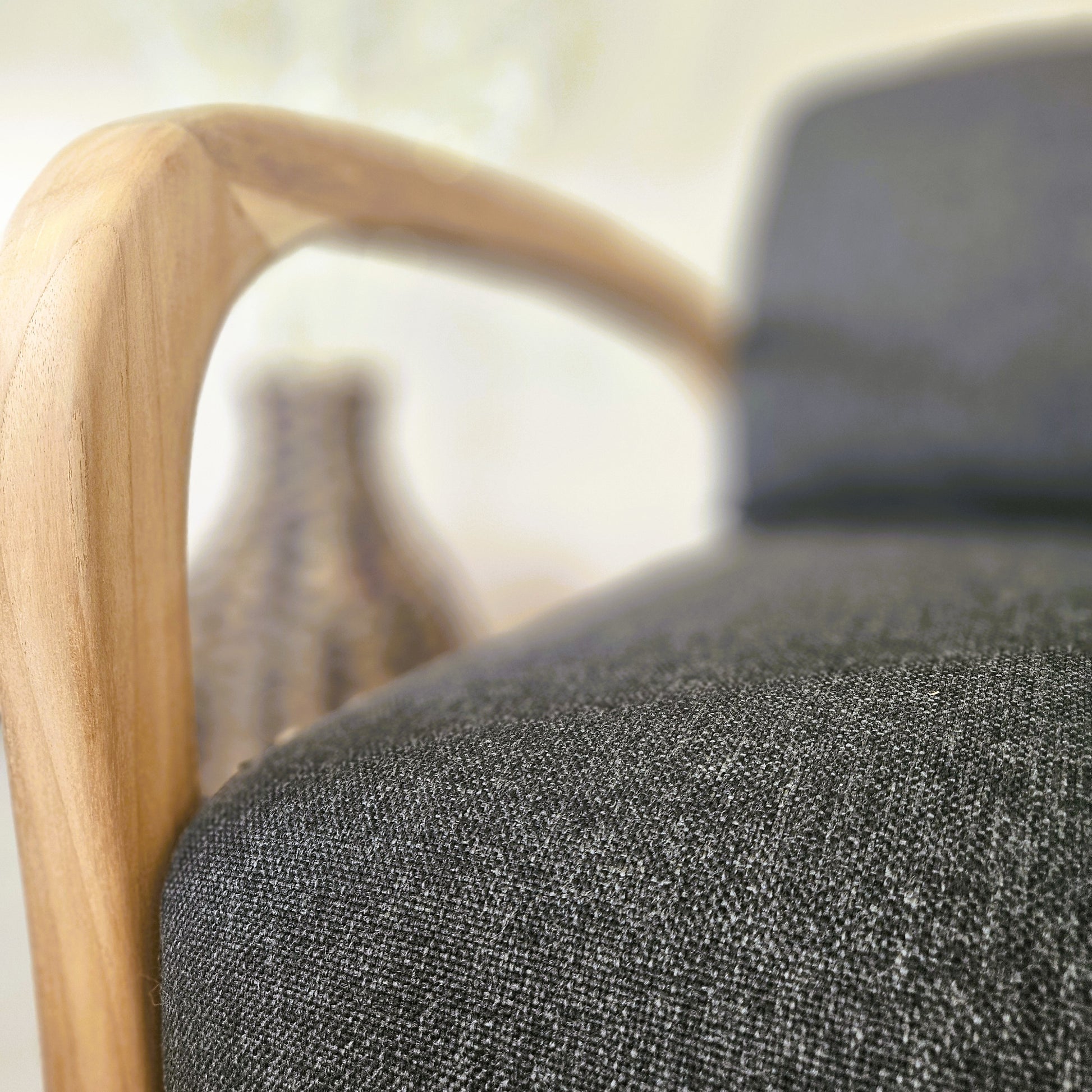 Close-up of a handcrafted wooden lounge chair featuring a smooth solid teak frame and textured dark upholstery fabric.