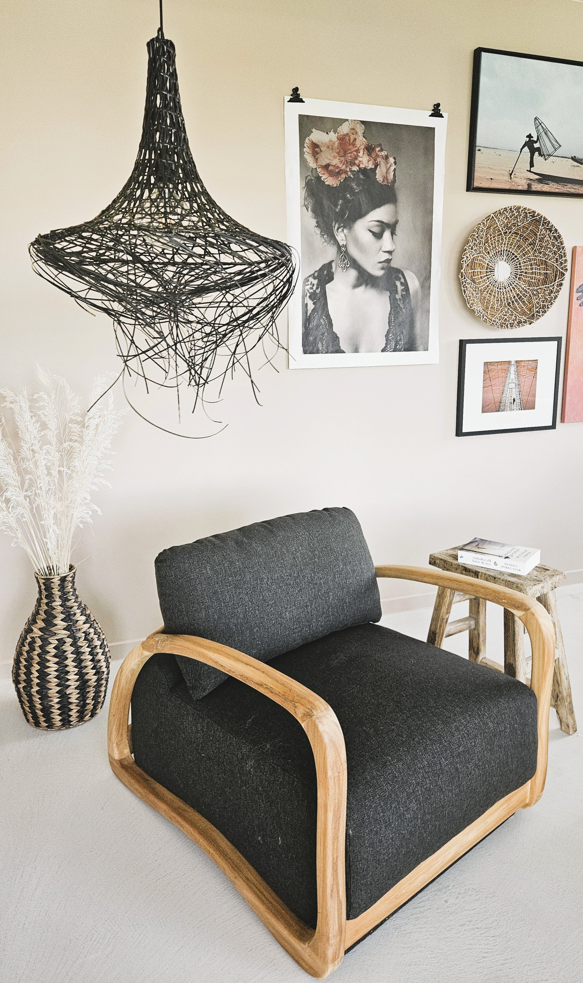 Handcrafted teak lounge chair with dark upholstery in a bohemian interior, styled with natural fiber décor, wall art and a woven pendant light.