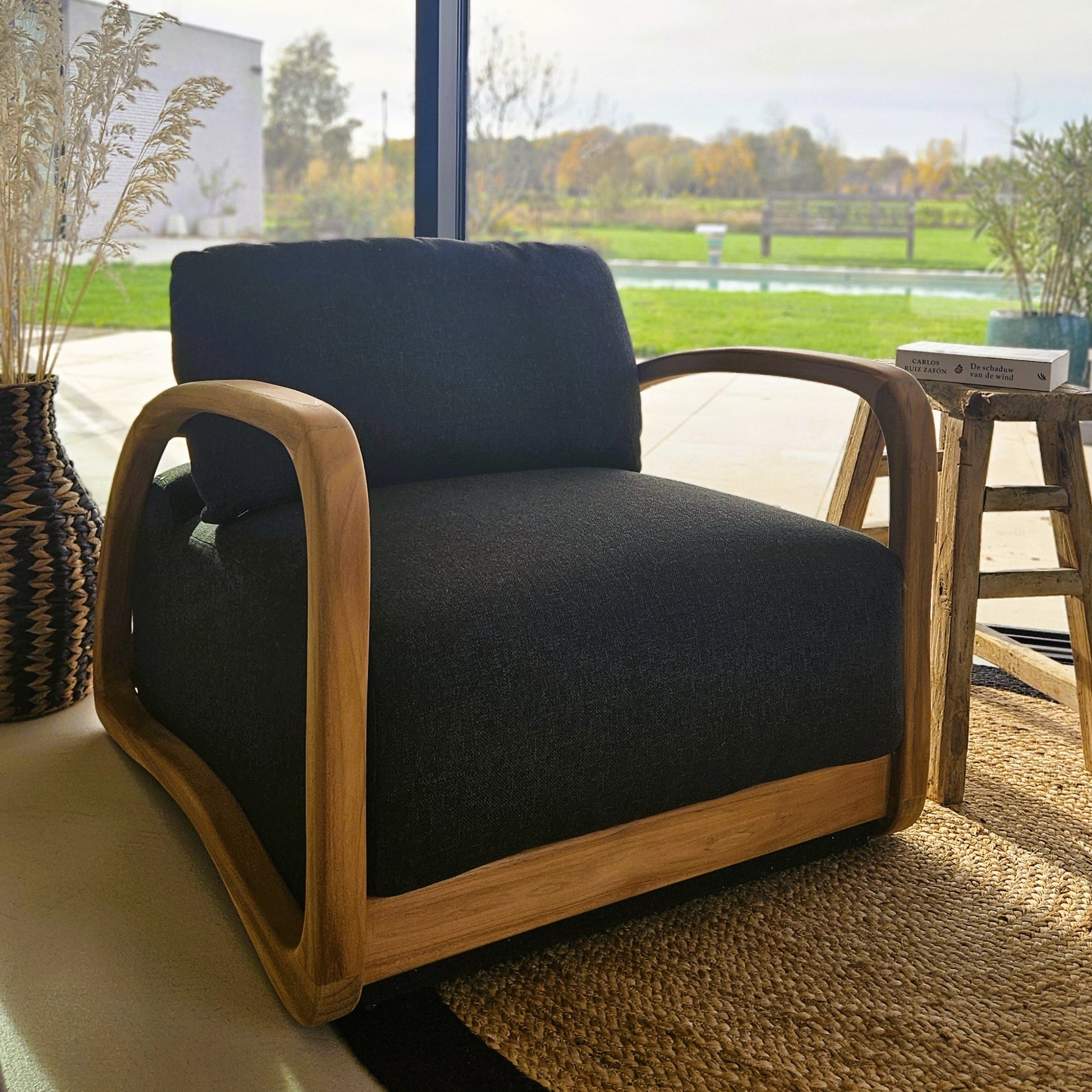 Handcrafted teak lounge chair with dark upholstery in a bright contemporary interior overlooking a garden and pool.