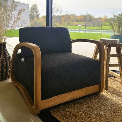 Handcrafted teak lounge chair with dark upholstery in a bright contemporary interior overlooking a garden and pool.