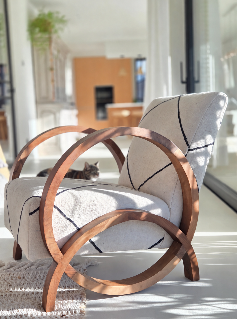 Fauteuil design avec une structure courbée en bois de noyer, un revêtement crème et un motif de lignes géométriques noires dans un intérieur moderne et lumineux