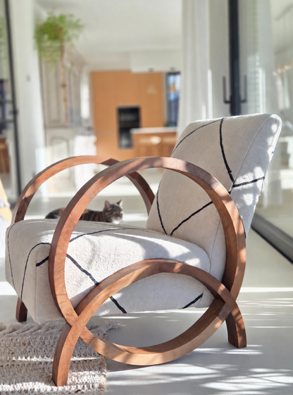 Fauteuil design avec une structure courbée en bois de noyer, un revêtement crème et un motif de lignes géométriques noires dans un intérieur moderne et lumineux