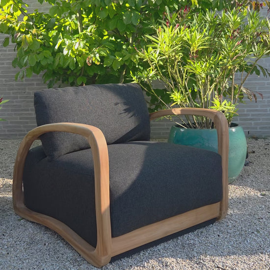 Video showcasing the Grade A Teak Luxury Lounge Chair  Adrian from multiple angles, featuring a solid Grade A teak frame and dark grey outdoor cushions in a contemporary Mediterranean setting
