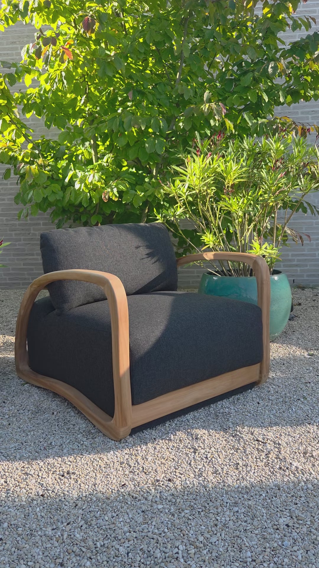 Video showcasing the Grade A Teak Luxury Lounge Chair  Adrian from multiple angles, featuring a solid Grade A teak frame and dark grey outdoor cushions in a contemporary Mediterranean setting