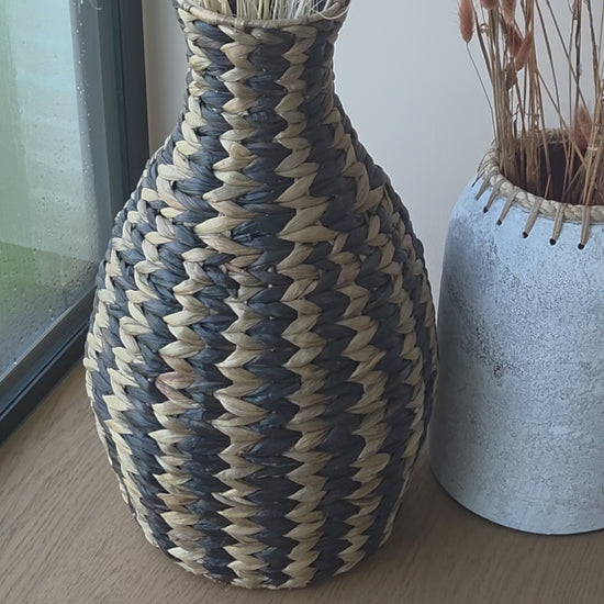 Zahara decorative woven vase featuring a striking black and natural zigzag pattern, styled with dried grasses. A textured statement piece that brings warmth and character to bohemian and contemporary interiors.